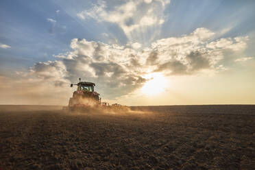 Traktor beim Pflügen und Kultivieren eines Feldes bei Sonnenuntergang - NOF00921