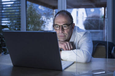 Freelancer wearing eyeglasses and having video call on laptop at home office - UUF31060