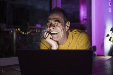 Älterer Mann lachend in der Nähe von Laptop zu Hause - UUF31081
