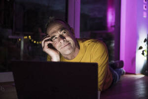 Thoughtful man lying on floor near laptop at home - UUF31082