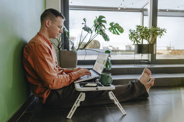 Freelancer sitting on floor and working on laptop - YTF01636