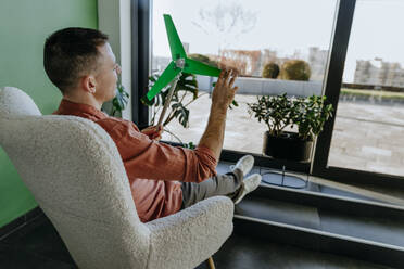 Freiberufler auf einem Sessel sitzend mit einem Windradmodell im Büro zu Hause - YTF01655