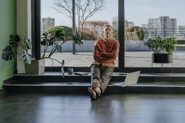 Freelancer resting with arms crossed on steps near glass door - YTF01669