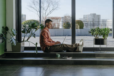 Freelancer working on laptop near glass door - YTF01670