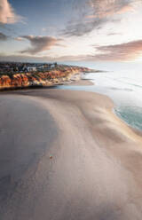 Luftaufnahme von Southport Beach und Klippen bei Sonnenuntergang, mit rosa Wolken und einem bunten Sonnenschirm am Strand. Onkaparinga, Südaustralien, Australien. - AAEF25239