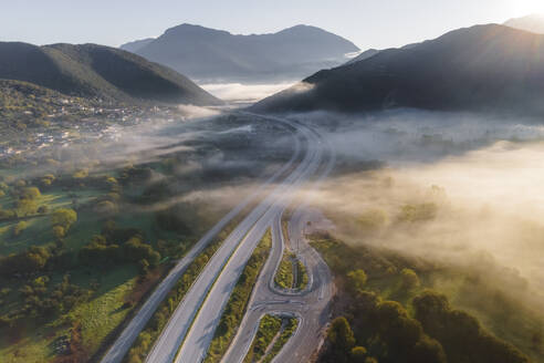 Luftaufnahme von Fahrzeugen auf der Autobahn bei Sonnenaufgang mit niedrigen Wolken und Nebel zwischen den Bergen in Psaka, Epirus, Griechenland. - AAEF25472