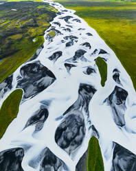 Luftaufnahme einer Drohne von Flussadern, die durch grünes Ackerland in Island fließen. - AAEF25922