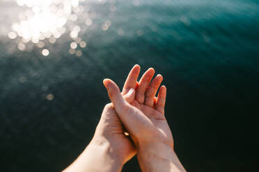 Zwei Hände, die sich sanft auf der glitzernden Oberfläche eines ruhigen, vom Sonnenlicht beleuchteten Gewässers berühren - ADSF52609