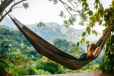 A peaceful scene of a person relaxing in a hammock surrounded by lush greenery and majestic mountains - ADSF52613