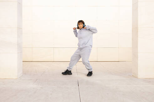 Junge Frau in bequemer Sportkleidung tanzt vor einem minimalistischen Hintergrund - ADSF52684