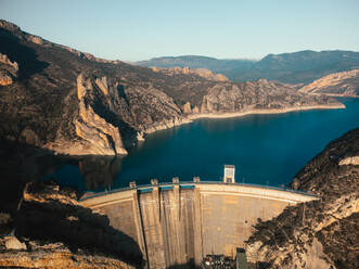 Aerial view of a large dam with full water levels in a mountainous region during golden hour - ADSF52693