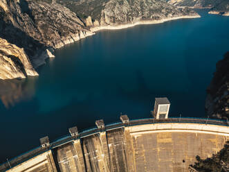 Top view of a dam with deep blue waters enclosed by steep cliffs under a golden sunlight - ADSF52695