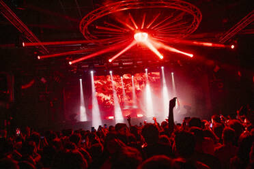 A bustling nightclub scene illuminated by a spectacular light show with vivid red hues and beams shining down - ADSF52712