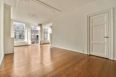 An elegant, empty living room featuring polished hardwood floors, large windows with curtains, and intricate ceiling molding. - ADSF52718