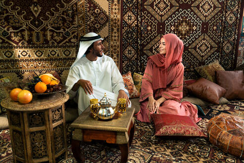 Junges Paar aus den Emiraten verbringt Zeit in einem traditionellen arabischen Café. Mann und Frau mit Kandura und Abaya aus Dubai unterhalten sich. - DMDF09283