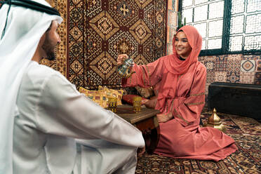 Junges Paar aus den Emiraten verbringt Zeit in einem traditionellen arabischen Café. Mann und Frau mit Kandura und Abaya aus Dubai unterhalten sich. - DMDF09295