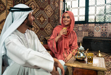 Junges Paar aus den Emiraten verbringt Zeit in einem traditionellen arabischen Café. Mann und Frau mit Kandura und Abaya aus Dubai unterhalten sich. - DMDF09297