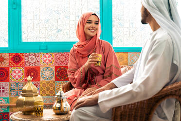 Junges Paar aus den Emiraten verbringt Zeit in einem traditionellen arabischen Café. Mann und Frau mit Kandura und Abaya aus Dubai unterhalten sich. - DMDF09300