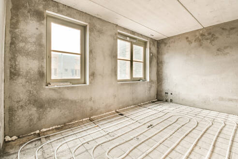 Ein unfertiger Raum mit Fußbodenheizung vor der Verlegung des endgültigen Bodens, mit Rohrleitungen und Beton. - ADSF52733