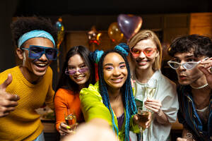 Eine Gruppe von Freunden feiert zu Hause am Neujahrsabend. Junge Frauen und Männer feiern in der Wohnung, trinken und essen, tanzen und haben Spaß. Konzept über Feiertage und Partys. - DMDF09305