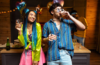 Eine Gruppe von Freunden feiert zu Hause am Neujahrsabend. Junge Frauen und Männer feiern in der Wohnung, trinken und essen, tanzen und haben Spaß. Konzept über Feiertage und Partys. - DMDF09311