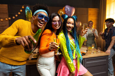 Eine Gruppe von Freunden feiert zu Hause am Neujahrsabend. Junge Frauen und Männer feiern in der Wohnung, trinken und essen, tanzen und haben Spaß. Konzept über Feiertage und Partys. - DMDF09333