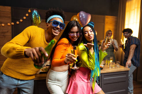 Eine Gruppe von Freunden feiert zu Hause am Neujahrsabend. Junge Frauen und Männer feiern in der Wohnung, trinken und essen, tanzen und haben Spaß. Konzept über Feiertage und Partys. - DMDF09334