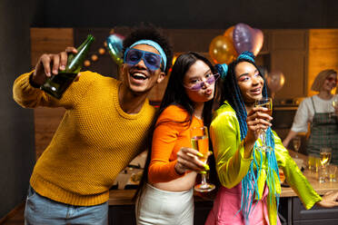 Eine Gruppe von Freunden feiert zu Hause am Neujahrsabend. Junge Frauen und Männer feiern in der Wohnung, trinken und essen, tanzen und haben Spaß. Konzept über Feiertage und Partys. - DMDF09335