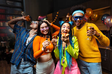Eine Gruppe von Freunden feiert zu Hause am Neujahrsabend. Junge Frauen und Männer feiern in der Wohnung, trinken und essen, tanzen und haben Spaß. Konzept über Feiertage und Partys. - DMDF09341
