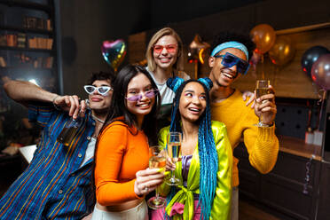 Group of friends making party at home on new year evening. Young women and men celebrating in the apartment drinking and eating, dancing and having fun. Concept about holidays and parties. - DMDF09344