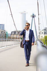 Geschäftsmann mit Smartphone beim Spaziergang auf einer Brücke in der Stadt - PUF02029