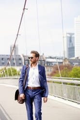 Geschäftsmann mit Sonnenbrille und Spaziergang auf einer Brücke in der Stadt - PUF02030