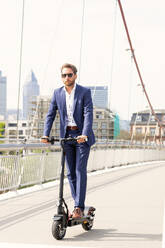 Businessman riding electric push scooter on bridge in city - PUF02031