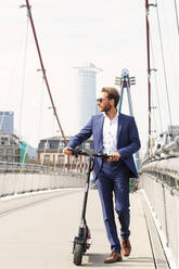 Businessman walking with electric push scooter on bridge in city - PUF02032