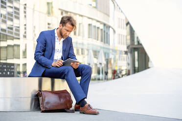 Businessman sitting on bench and using tablet PC in the city - PUF02039