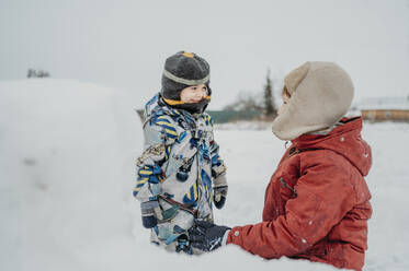 Geschwister tragen warme Kleidung und spielen im Schnee - ANAF02659