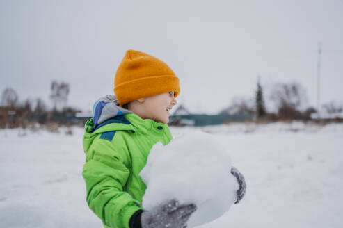 Lächelnder Junge mit Schneeball im Winter - ANAF02662