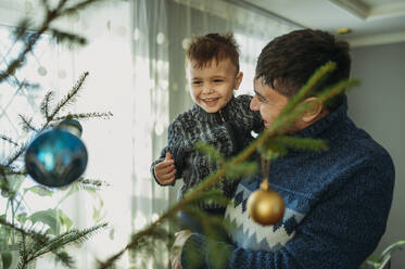 Happy father carrying son near Christmas tree at home - ANAF02663