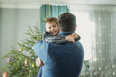 Father embracing son in arms at home - ANAF02668