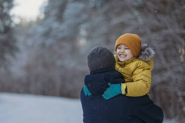 Father carrying playful son in winter forest - ANAF02689