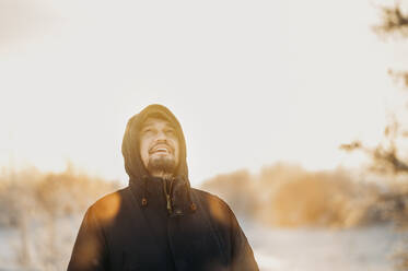 Älterer Mann mit Winterjacke im Wald an einem sonnigen Tag - ANAF02697