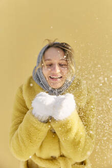 Glückliche junge Frau, die Schnee hält und vor einer Mauer steht - SANF00165