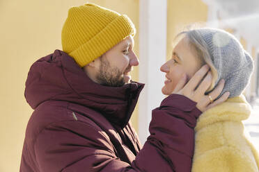 Glücklicher Mann umarmt Frau im Winter an einem sonnigen Tag - SANF00168