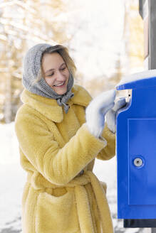 Glückliche junge Frau wirft Postkarte in Briefkasten - SANF00169