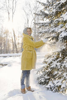 Glückliche junge Frau, die eine Tanne im Winter berührt - SANF00174