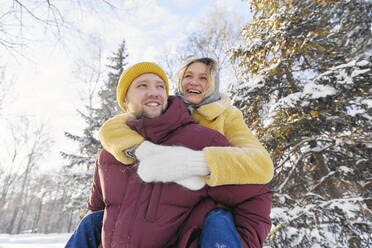 Happy man giving piggyback ride to young woman in winter forest - SANF00180