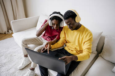 Junge Freunde tragen kabellose Kopfhörer und benutzen einen Laptop zu Hause - NLAF00212