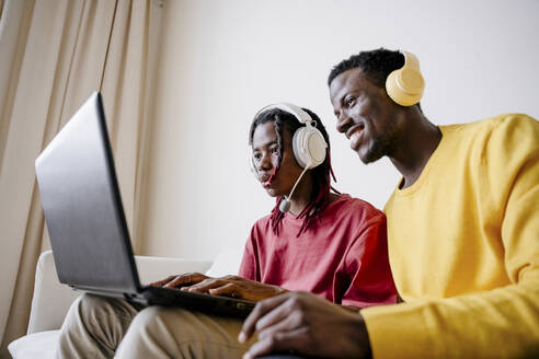 Freunde tragen kabellose Kopfhörer und benutzen einen Laptop zu Hause - NLAF00213