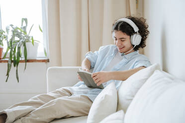 Lächelnder Mann mit Headset und Tablet-PC auf dem Sofa zu Hause - NLAF00229