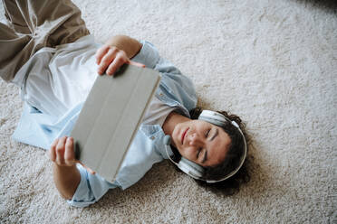 Man lying on carpet and using tablet PC at home - NLAF00232